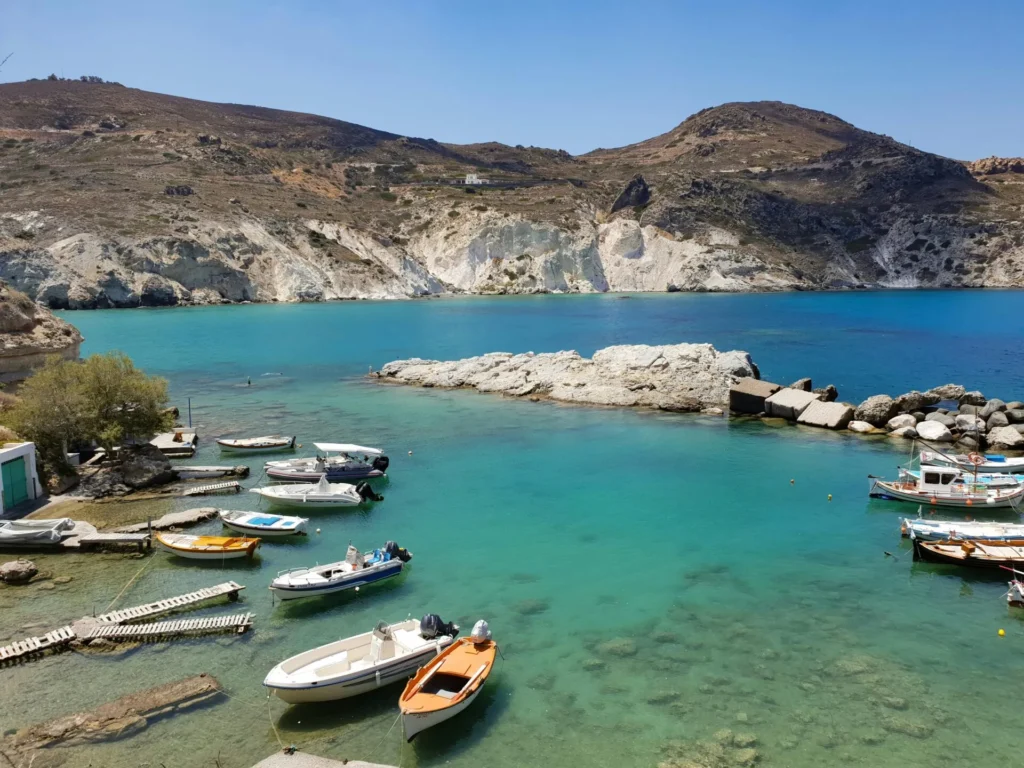 Sailboat anchored in turquoise bay below white Cycladic village at sunset